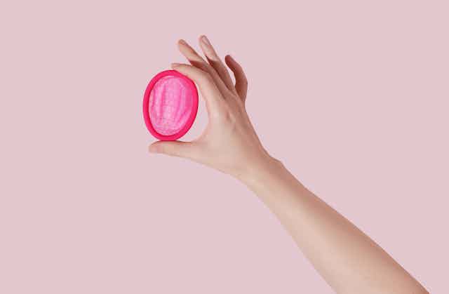 hand holds pink menstrual disc
