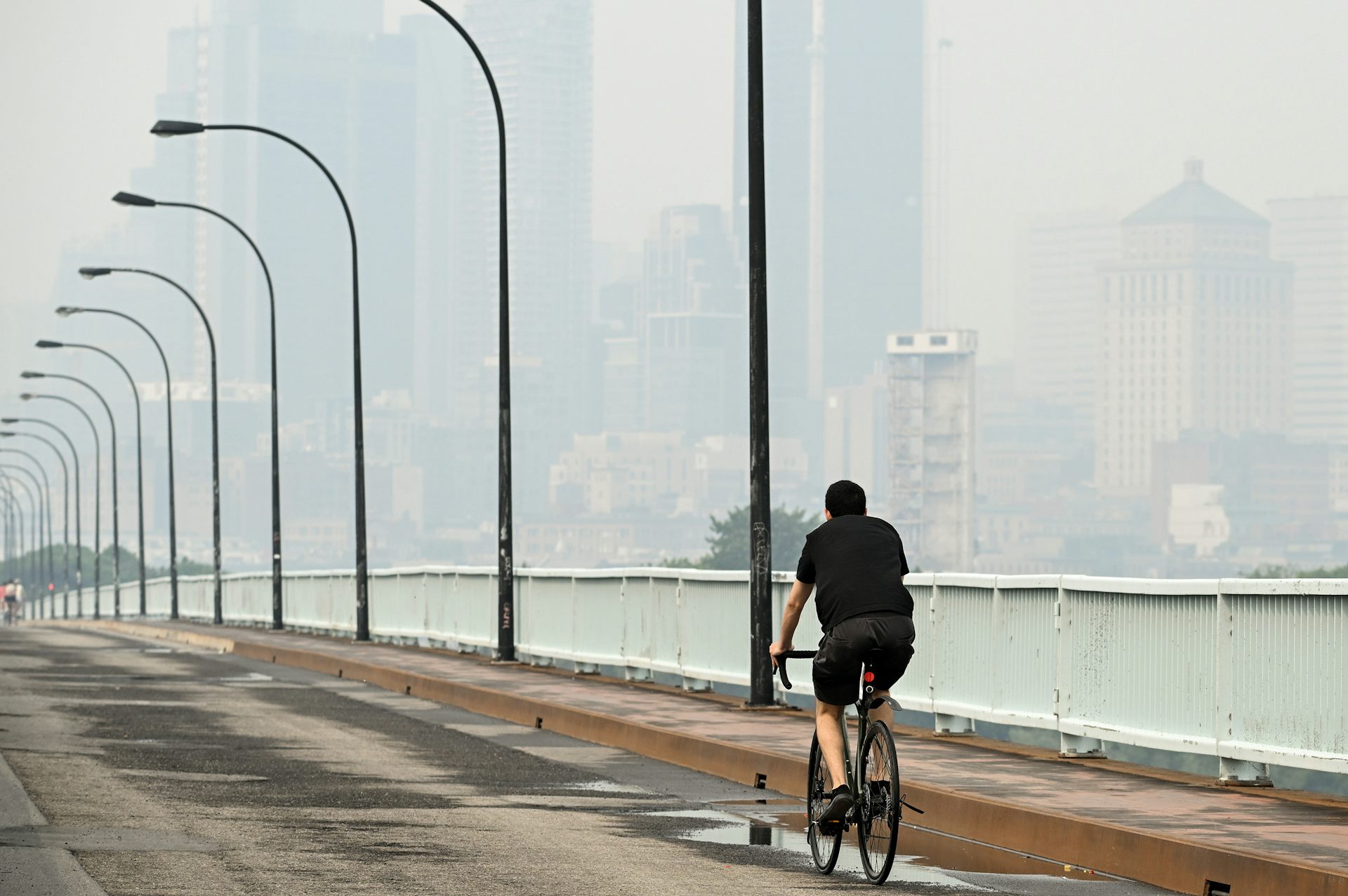 A cyclist is seen against a hazy, smoke-obscured city skyline