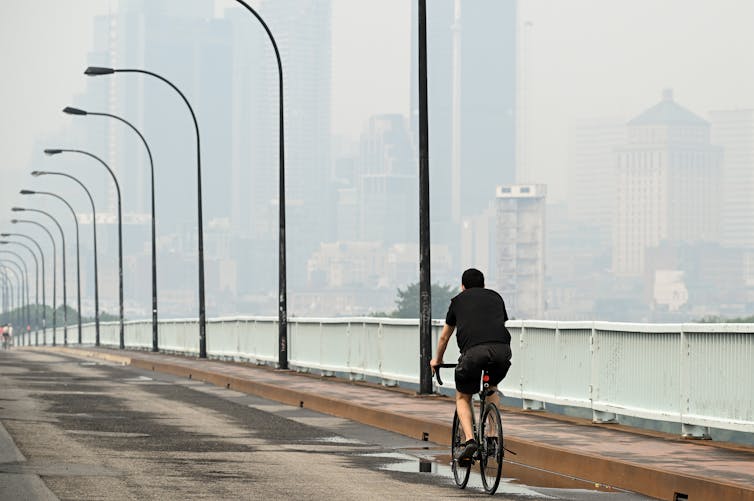A cyclist is seen against a hazy, smoke-obscured city skyline