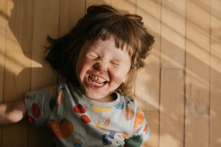 girl lies on floorboard with big grin, eyes closed