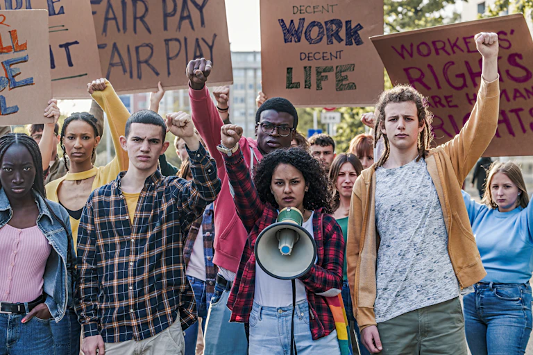 Group of people with fists raised and stern facial expressions holding signs about fair pay.
