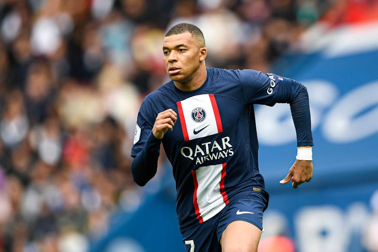 Man in blue uniform running, blurred crowd in the background.