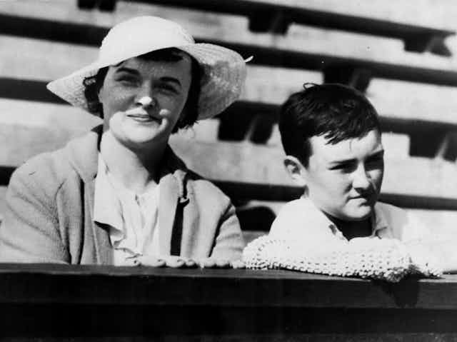 Foto en blanco y negro de una mujer con sombrero posando con un niño en las gradas.