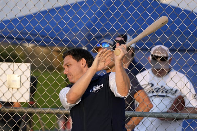 A man in a vest swings a baseball bat.