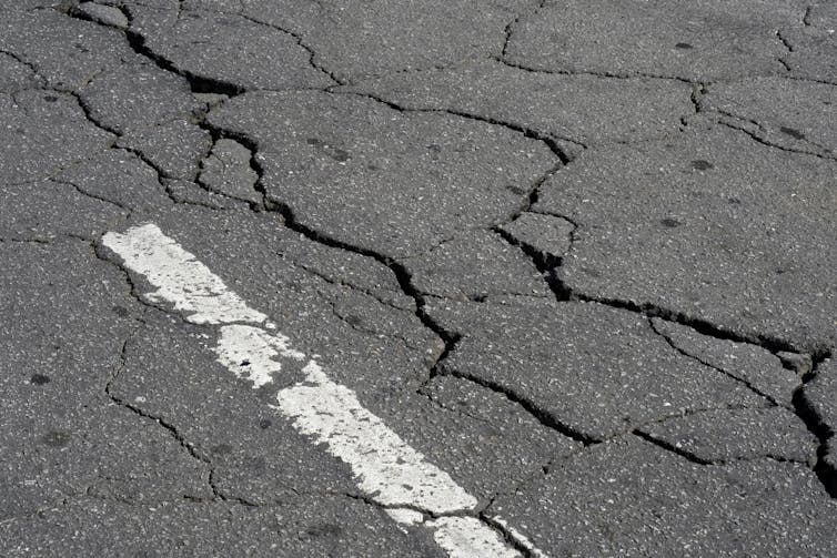 A close-up of a street with several cracks running through the asphalt and a white paint stripe.