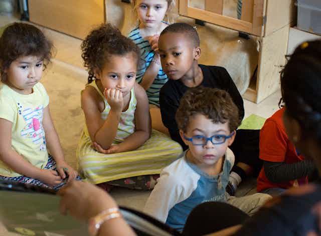 Children sitting on the floor listening as an educator reads.