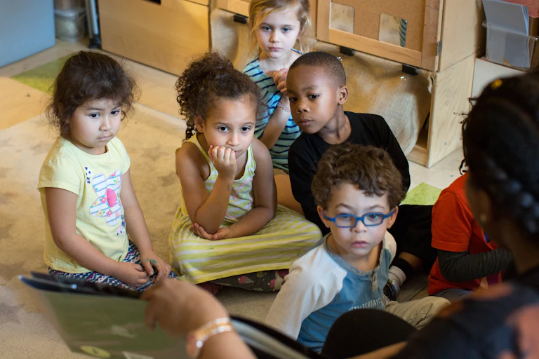 Children sitting on the floor listening as an educator reads.
