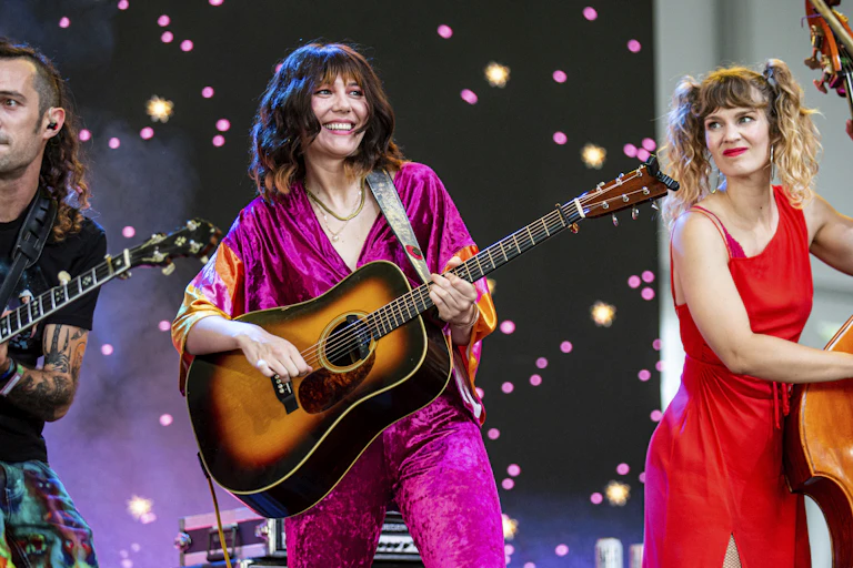 A woman holding an acoustic guitar flanked by a woman holding an upright bass and a man holding a banjo