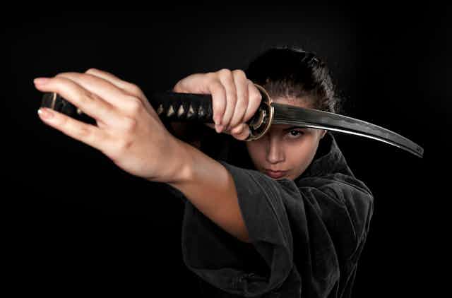 A woman with a serious look on her face uses two hands to hold a Japanese sword.