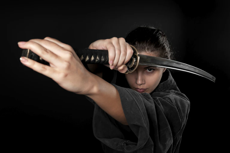 A woman with a serious look on her face uses two hands to hold a Japanese sword.