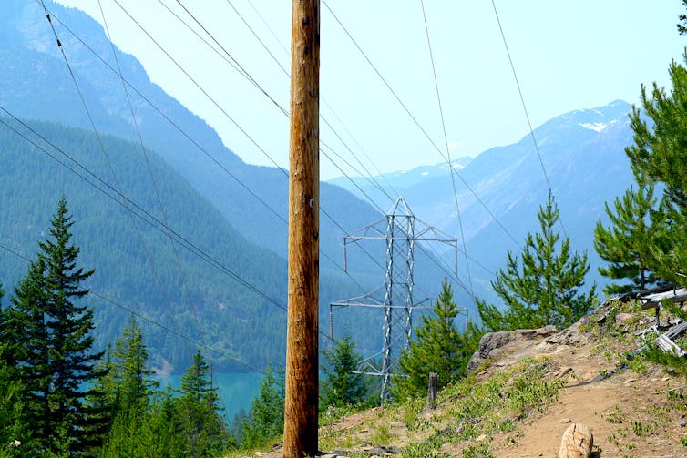 Powerlines along a rugged mountainside with a lake and forest in the background.