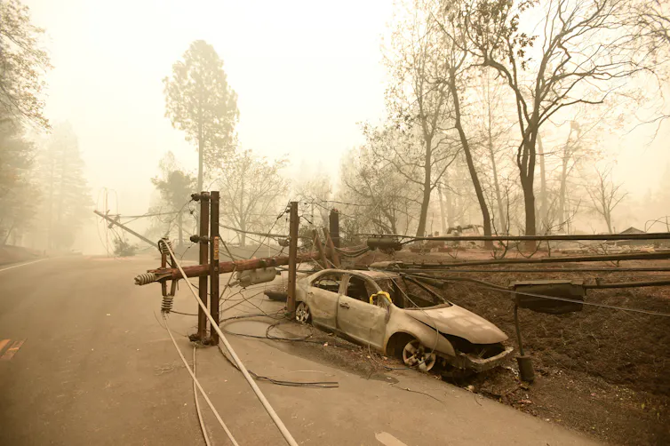 A burned powerline lays across a burned-out car in a burned scene with a smoky yellow-orange glow.