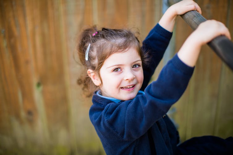 A young girl hangs from a monkey bar.