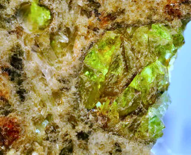 A close up photo of a lump of rock containing green crystals.