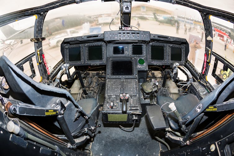 A wide angle view of a cabin with two seats and a series of screens and complex controls in front