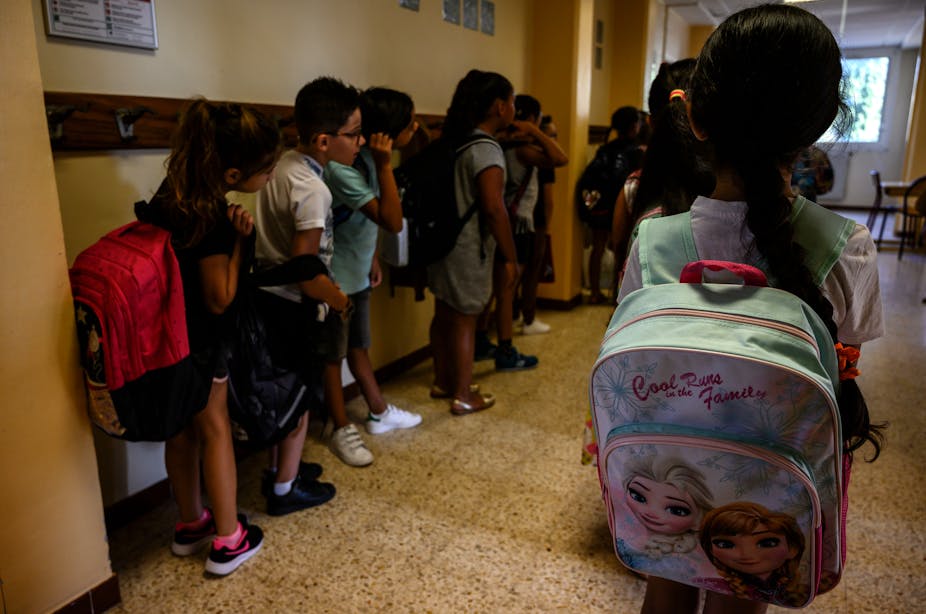 Des élèves attendent d'entrer dans leur classe avec leurs cartables sur le dos le jour de la rentrée