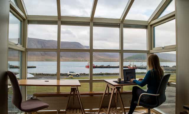 A woman working on her laptop in front of a big window with views.