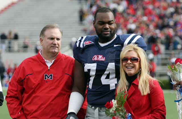 In this 2008 photo, University of Mississippi football player Michael Oher poses before a game with Sean and Leigh Anne Tuohy. Oher is wearing his football jersey; the Touhys, flanking him, are both wearing red In support.