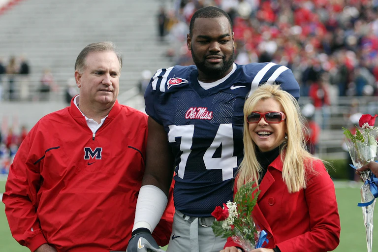 In this 2008 photo, University of Mississippi football player Michael Oher poses before a game with Sean and Leigh Anne Tuohy. Oher is wearing his football jersey; the Touhys, flanking him, are both wearing red In support.