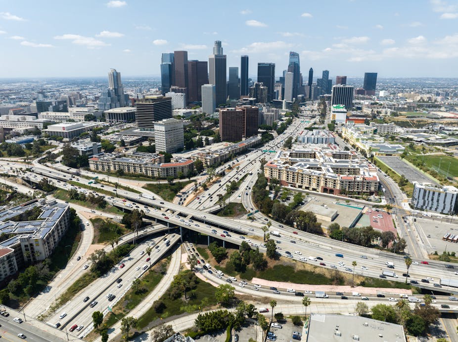 An aerial view shows a small cluster of sky scrapers and large freeways, intersecting. 