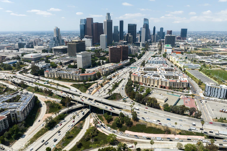 An aerial view shows a small cluster of sky scrapers and large freeways, intersecting.