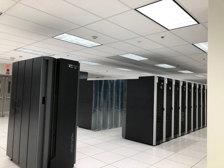 A white room filled with large black data servers, which look like lockers.