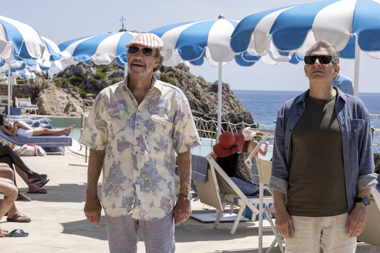 Two men seen in front of white and blue beach umbrellas.