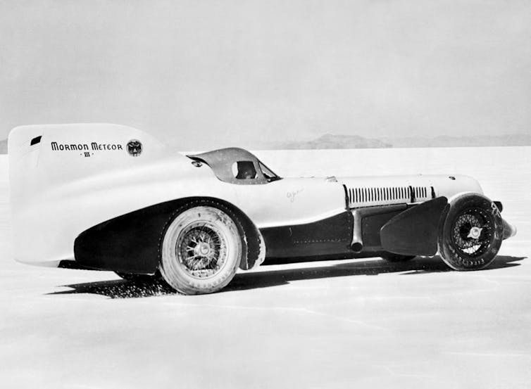 A black and white image of an old-fashioned car against a white, flat landscape.