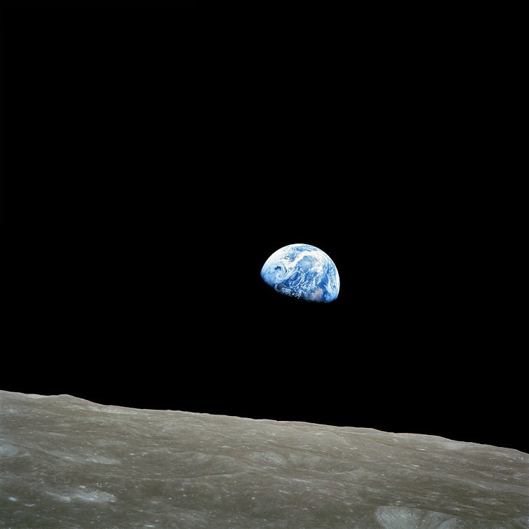 Blue and white Earth, half-obscured by shadow, seen hanging in darkness over a stark lunar landscape.