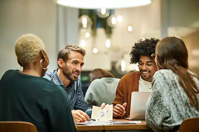 four people of diverse backgrounds sit at a table and work
