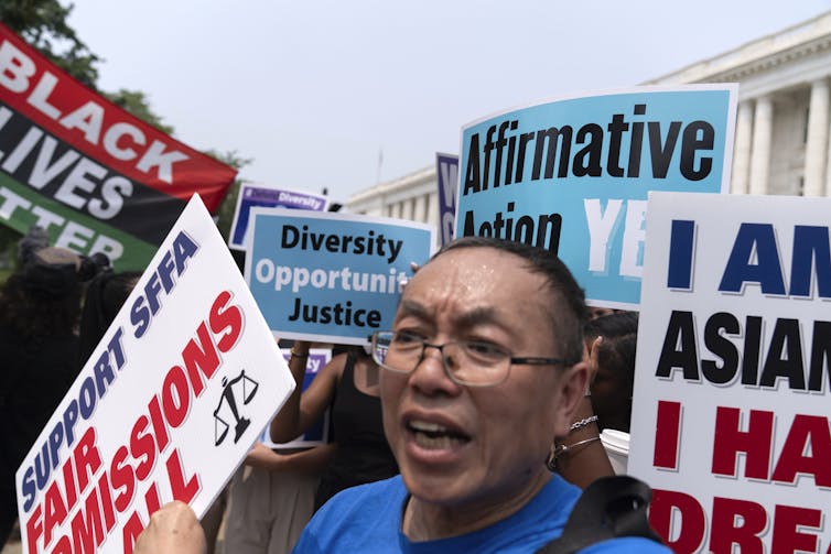 a woman holding a sign protests outside of the Supreme Court building amid several other affirmative action-related signs