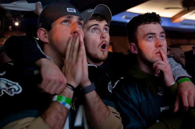 Three male football fans express amazement while watching the Super Bowl.
