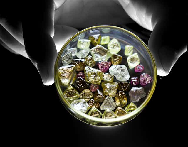 Photo of a hand holding a dish of rough diamonds of various colours