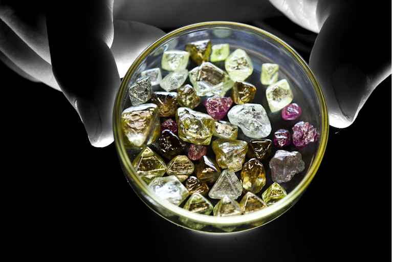 Photo of a hand holding a dish of rough diamonds of various colours