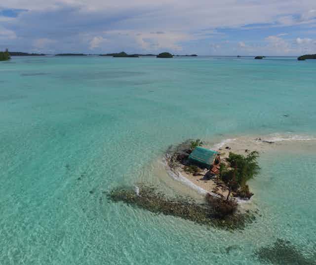 Aerial photograph showing sea water surrounding a hut and trees on a tiny island, o illustrate how sea level rise impacting the Solomon Islands