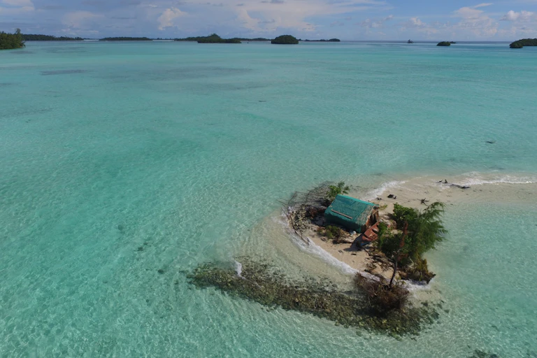 Aerial photograph showing sea water surrounding a hut and trees on a tiny island, o illustrate how sea level rise impacting the Solomon Islands