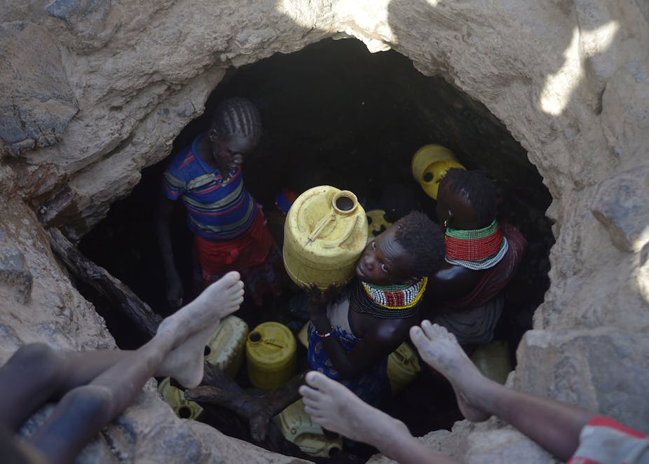 A young girl passes up a jerrycan filled with murky water trickling into a waterhole