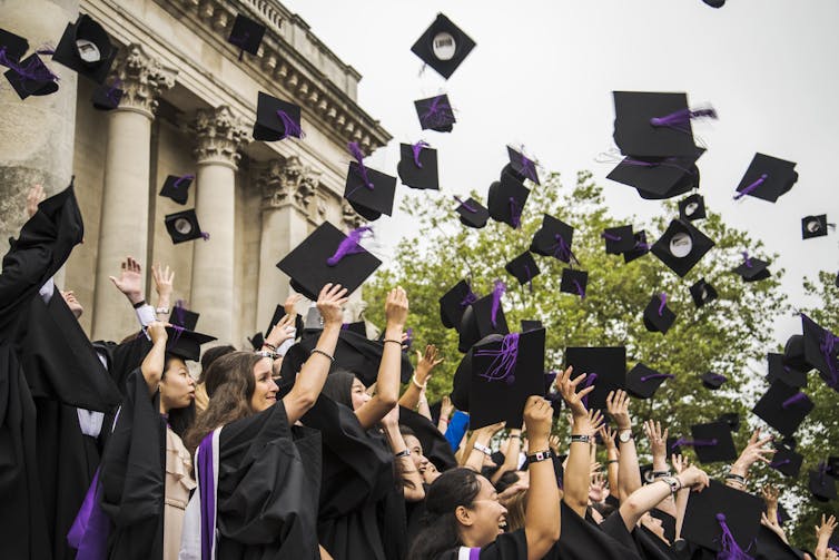 Students wearing black gowns throw their mortar board hats in the air.
