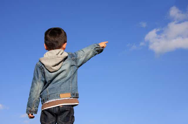 Un niño de espaldas apunta con la mano al cielo.