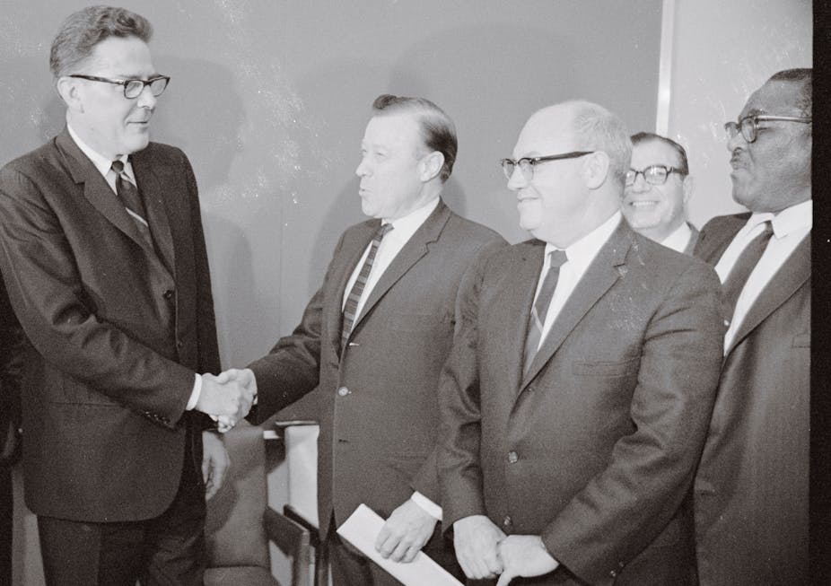 Men in suits shake hands in an old black-and-white photo.