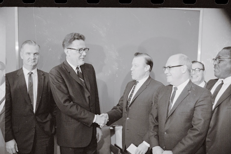 Men in suits shake hands in an old black-and-white photo.