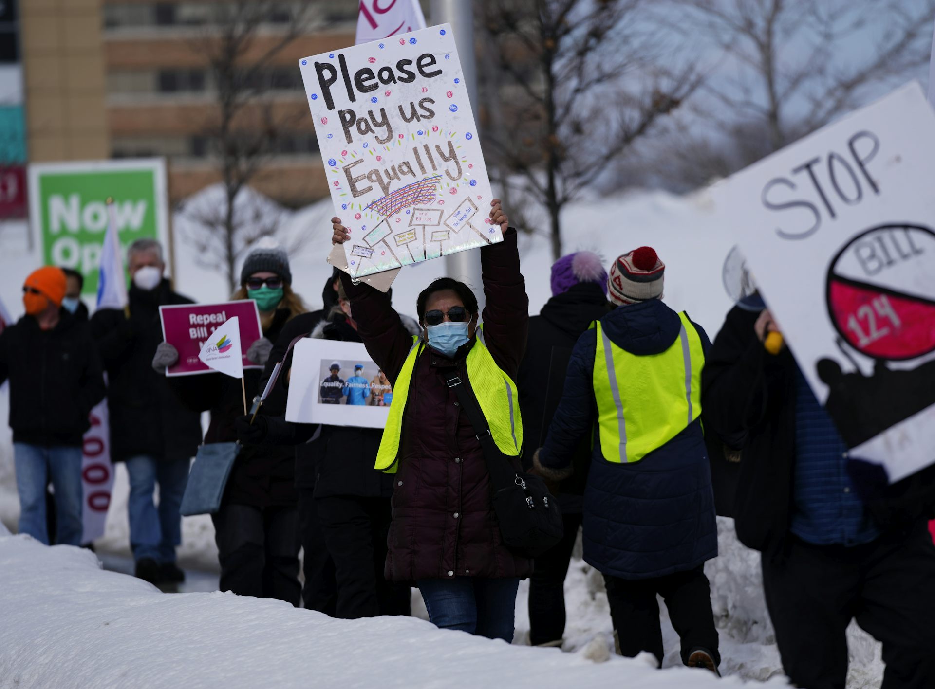 People seen on a picket line, one with a sign that says 'please pay us equally.'