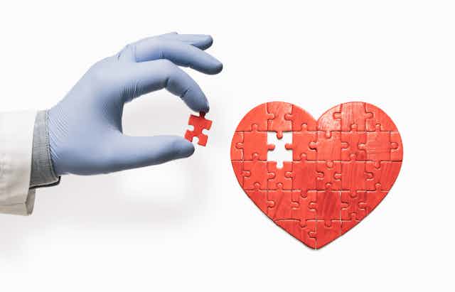 Gloved hand holding the missing puzzle piece to a red heart puzzle