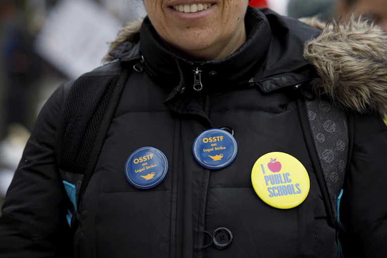 Buttons on a coat say I love public schools and OSSTF on legal strike.