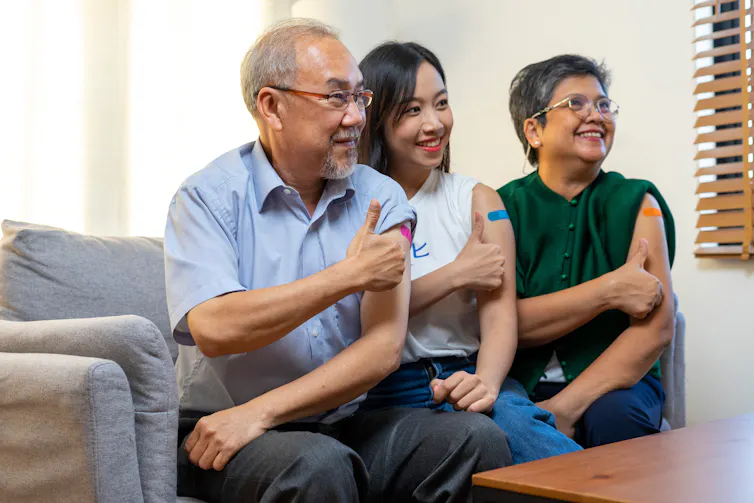 An older couple and a teen sitting on a sofa showing vaccination bandages on their upper arms