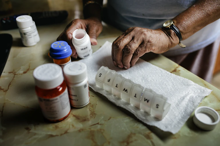 Closeup of the hands of a senior person holding a pill bottle with other pill bottles in the foreground.