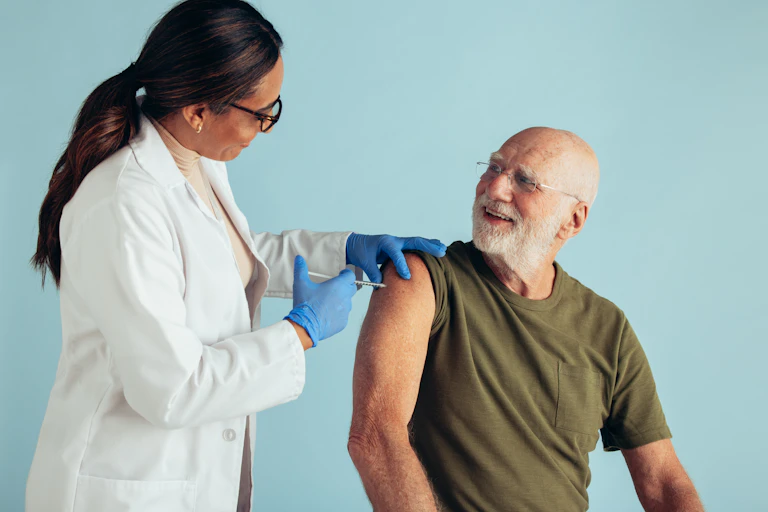 An older man in a green t-shirt getting a injection from a female doctor in a white coat and blue gloves