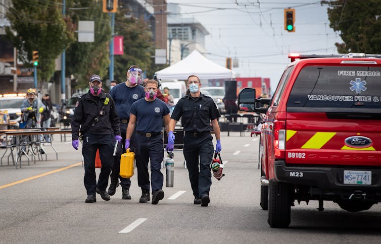 First responders carrying equipment walk down a street towards their vehicle.