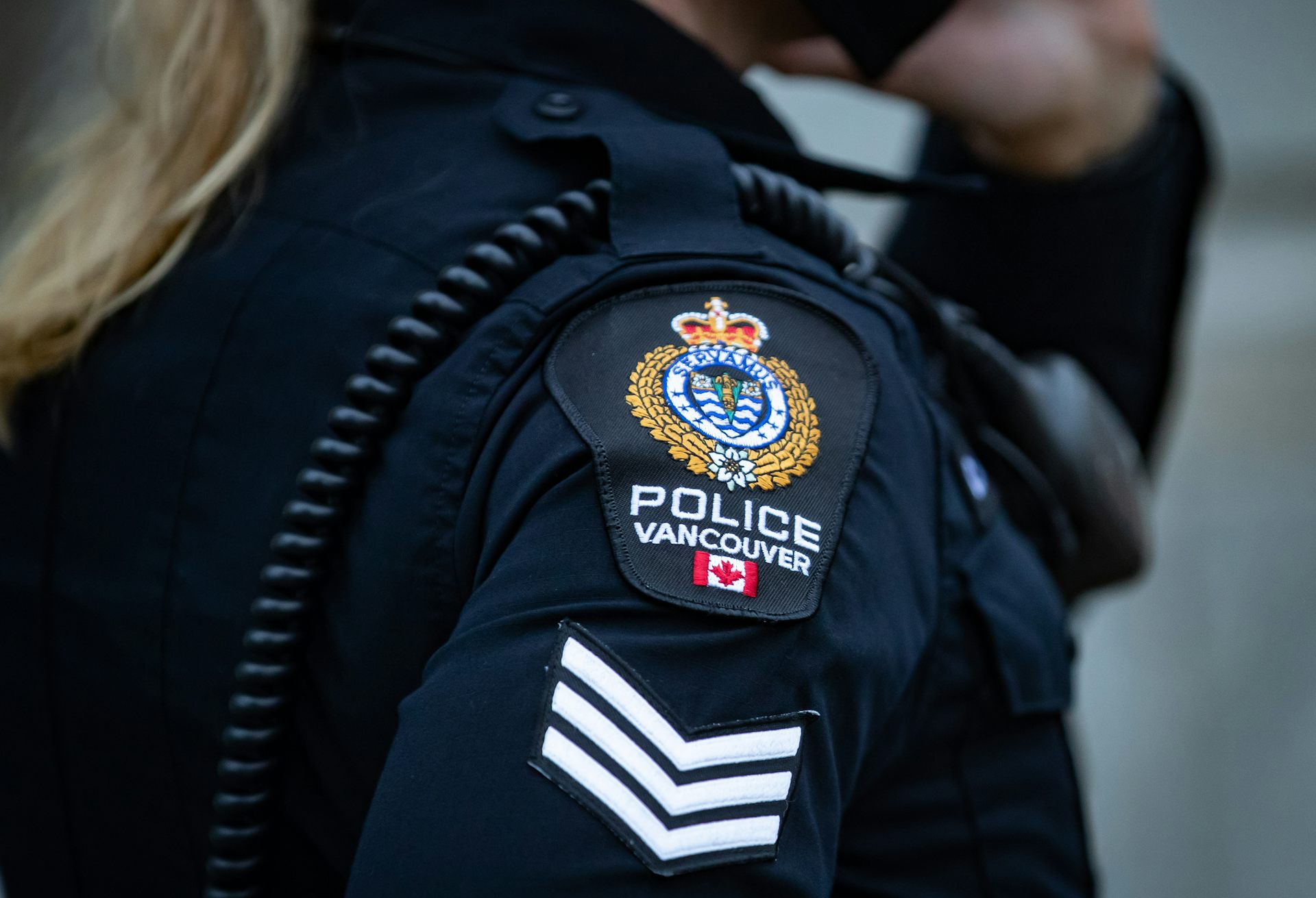 Close-up view of a woman's shoulder with a uniform patch with three chevrons and a crest reading Police Vancouver.