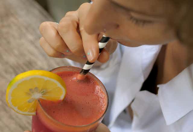 A woman drinking a smoothie through a paper straw.